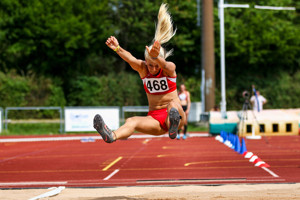 Female athlete mid-air during a long jump event, wearing red sportswear and number 468.